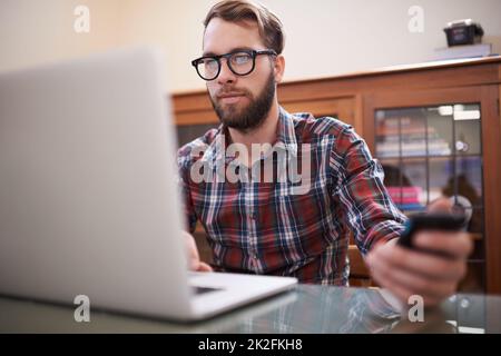 Using all the latest tech. a handsome young hipster working on a laptop. Stock Photo