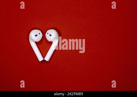 white wireless headphones lie on a red isolated background in the form of a heart top view. concept of communication, technology, love. space for text. international world music day and valentine day Stock Photo