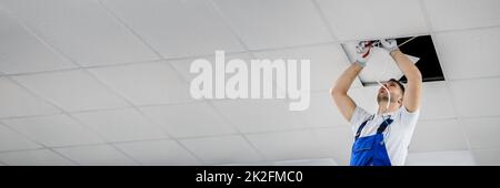 Electrician On Stepladder Installs Lighting To The Ceiling Stock Photo