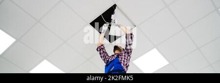 Electrician On Stepladder Installs Lighting To The Ceiling Stock Photo