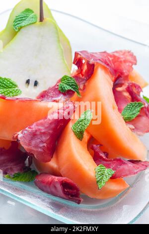 melon cantaloupe and pear with  proscutto and mint leaves Stock Photo