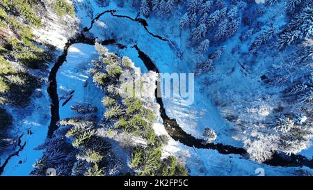 Aerial shot with drone of snowy forest with stream in winter Stock Photo