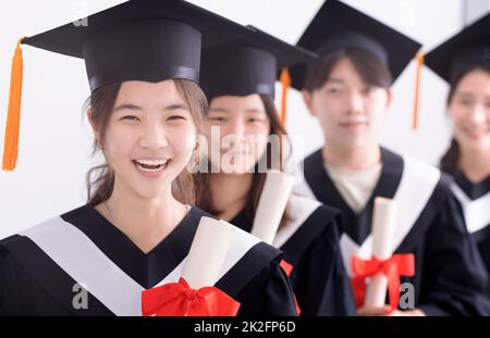 Successful graduation from university. Smiling beautiful Asian girl  university or college graduate standing with diploma over university at  background. Stock Photo