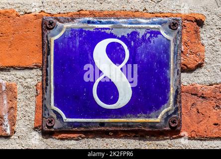 Old brick wall. Texture of old weathered brick wall with a number 8 on a blue sign. Stock Photo