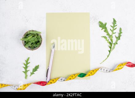 Planning a diet, arugula salad and tailor tape measure around the empty paper, healthy food and lifestyle, loosing weight Stock Photo