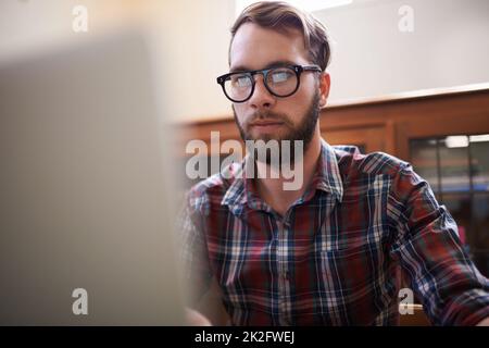 Using all the latest tech. a handsome young hipster working on a laptop. Stock Photo