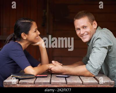 I am the luckiest guy on earth. A cute multi-racial couple sitting and holding hands while on a date. Stock Photo