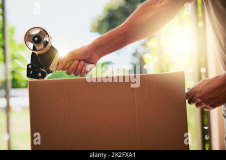 The very last box.... Closeup shot of an unrecognizable man closing a cardboard box with tape. Stock Photo