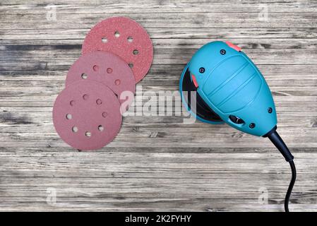 Orbital sander machine with sanding discs on wooden background. Adhesive sanding disks and palm sander for polishing and grinding. Stock Photo