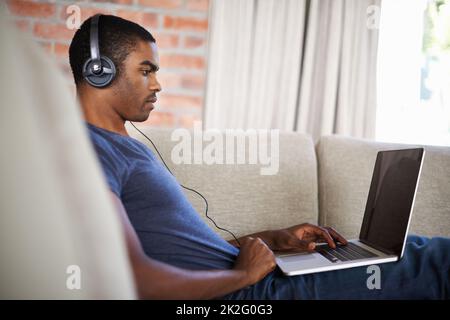 Focused on his work. a handsome young man using his laptop while relaxing at home. Stock Photo