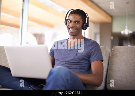 Watching a few videos during some free time. a handsome young man using his laptop while relaxing at home. Stock Photo
