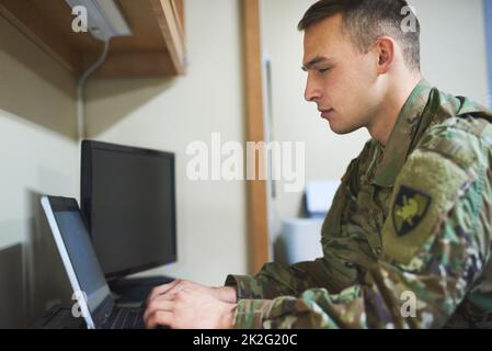 Army life, its not all guns and grenades. Shot of a young soldier using a laptop in the dorms of a military academy. Stock Photo