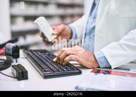 This will fix you up. Shot of a unrecognizable pharmacist typing on a computer keyboard while holding a medication subscription. Stock Photo