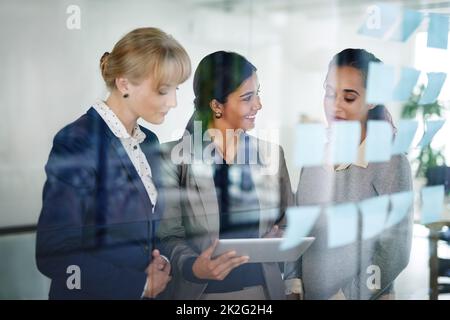 Work in progress. Cropped shot of a group of businesswomen working together on a digital tablet in an office. Stock Photo
