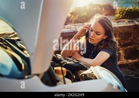 The engine just wont start. Cropped shot of a young woman calling roadside assistance after breaking down. Stock Photo