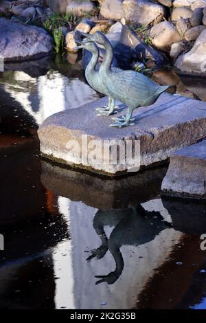 zwei dekorative Enten aus Metall spiegeln sich im Gartenteich Stock Photo