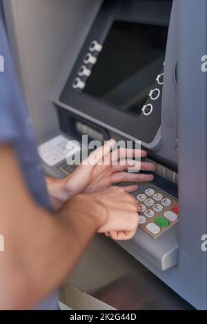 Keeping his pin code a secret. Cropped shot of a man entering his secret pin code at an ATM. Stock Photo