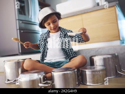Unleashing an epic drum solo. Shot of a happy little boy playing drums with pots on the kitchen floor while wearing a bowl on his head. Stock Photo