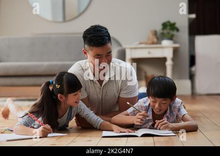 Spending time with my children. Shot of a cheerful father and his two children doing homework together while lying on the floor at home during the day. Stock Photo