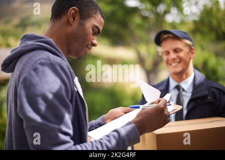 Checking the fine print. a handsome young man signing a form for a courier. Stock Photo
