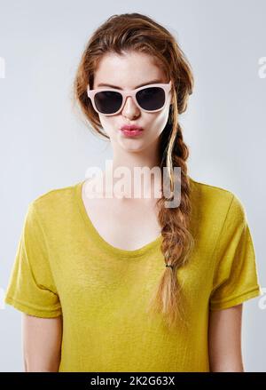 Simply fabulous. Studio portrait of an attractive young woman wearing trendy sunglasses isolated on gray. Stock Photo