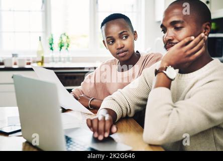 These bills are really stressing him out. Shot of a young couple looking stressed while going over their finances on a laptop at home. Stock Photo