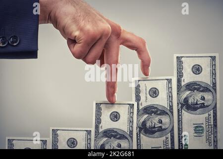 Working his way up to becoming a rich succesful business man. Close up concept shot of fingers walking crawling up a pile of one hundred dollar bills. Stock Photo