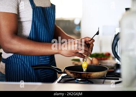 Fried eggs are his favourite. Cropped shot of an unrecognizable man frying eggs while making breakfast in his kitchen at home. Stock Photo