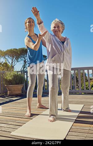 Improving health in the golden years. Shot of a senior woman doing yoga with an instructor on a patio outside. Stock Photo