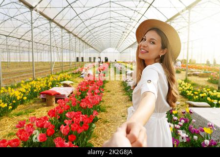 Follow me between tulips in spring time. Young woman holding man hand smiling looking back between rows of tulip flowers. Stock Photo