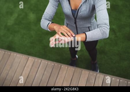 Set the time aside to get to your goals. High angle shot of a sporty young woman checking her watch while exercising outdoors. Stock Photo