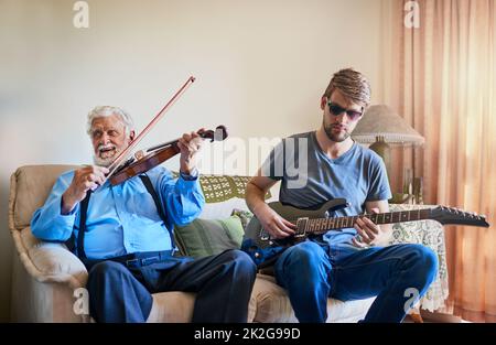 Music bridges the generation gap. Shot of a young man playing the electric guitar while his elderly grandfather plays the violin on the couch. Stock Photo