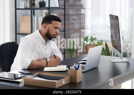 Sitting down for some thorough planning. Shot of a young businessman writing notes while working on a laptop in an office. Stock Photo