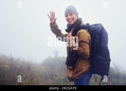 I dare you to keep up with me. a happy young female hiker waving at the camera. Stock Photo