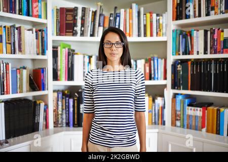 Its a privilege to be surrounded by books. an attractive young woman standing in her home library. Stock Photo