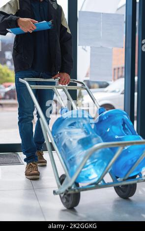 Bottled and delivered straight to your door. Cropped shot of a courier making a bottled water delivery in an office. Stock Photo