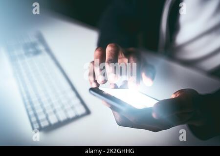 Checking the project timeline. High angle shot of an unrecognizable man using a cellphone while working late in the office. Stock Photo