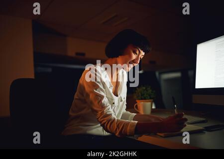 Making the night a productive one. Shot of a young businesswoman writing in a notebook during a late night at work. Stock Photo