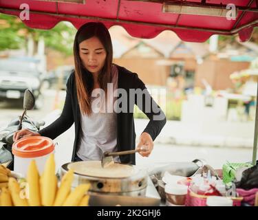 Coming right up. Shot of a food vendor in Thailand preparing a tasty snack. Stock Photo
