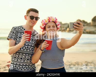 Summer vacay selfie time. Shot of a young couple hanging out at the beach. Stock Photo