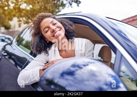 Feeling the wind in her hair. Shot of an attractive young businesswoman leaning out of her window while driving to work on her morning commute. Stock Photo