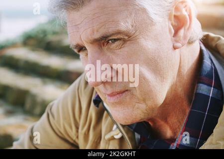 Sometimes you just have to sit down and reminisce. Closeup shot of an elderly man looking thoughtful while relaxing outdoors. Stock Photo