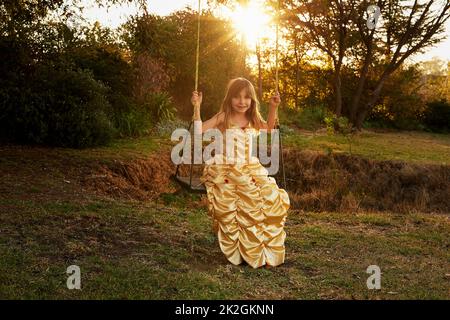 Shes dressed up for a day of fun. Portrait of a little girl dressed up as a princess sitting on a swing outside. Stock Photo