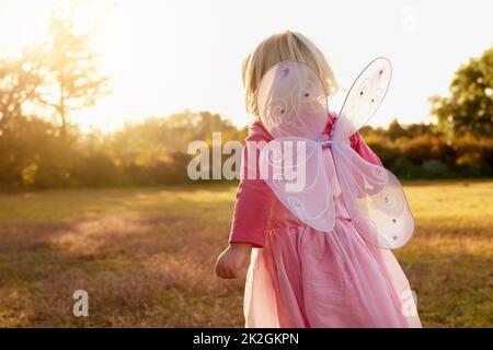 Children explore the world through the power of their imagination. Rear view shot of a little girl dressed up as a fairy enjoying the day outside. Stock Photo