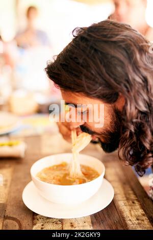 Enjoying a bowl full of noodles. Shot of a young man eating a bowl of noodles in a restaurant in Thailand. Stock Photo