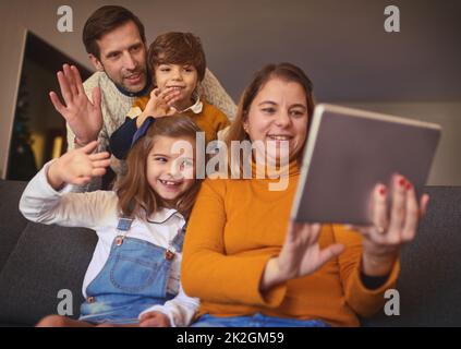 Were all here. Cropped shot of an affectionate young family of four video chatting using a digital tablet on the sofa at home. Stock Photo