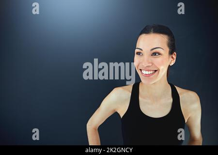 Being fit feels good. Shot of a sporty young woman posing against a dark background. Stock Photo