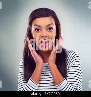 Wow what a pleasant surprise. Shot of a young woman posing against a grey background. Stock Photo