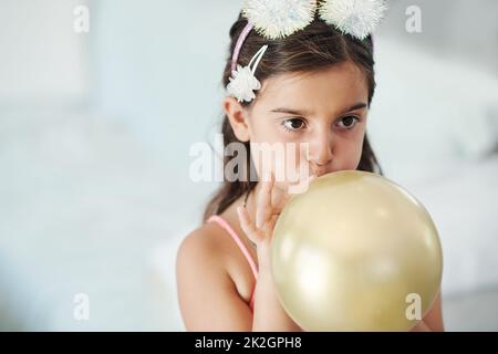 I want to see how big it gets. Shot of an adorable little girl blowing up a balloon at her birthday party. Stock Photo