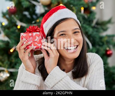 Does it make a sound. Shot of a young woman holding a gift at home. Stock Photo